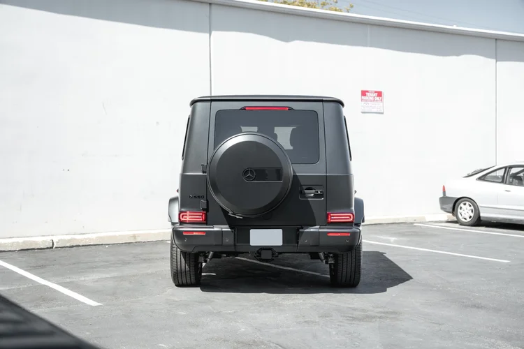 Complete straight rear view of the G 550 with its G 550 badge, round spare-wheel cover and red lamps against a white wall