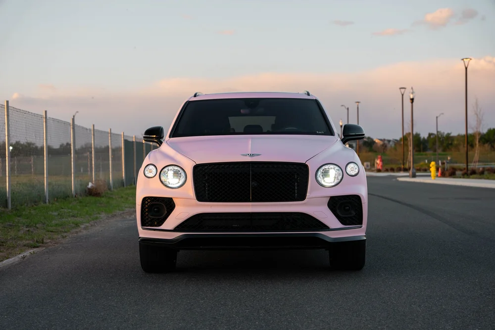 Centered full front view of the Sakura Pink Bentayga with its illuminated round headlights and black mesh grille