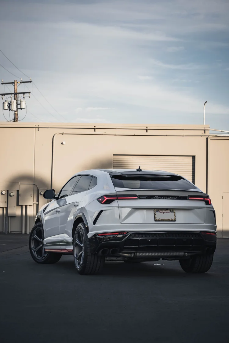 Complete white Urus from the rear in a tall frame, with red lamps and dark lower trim beneath a blue sky.