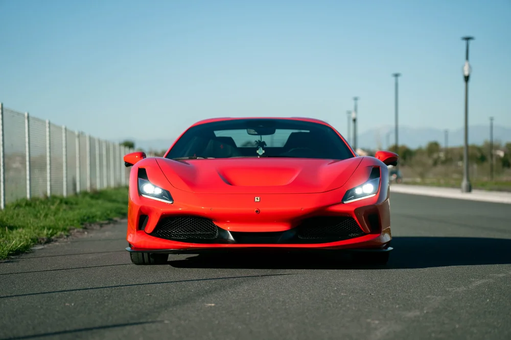 Complete straight front view of the red Ferrari F8 with both headlights illuminated