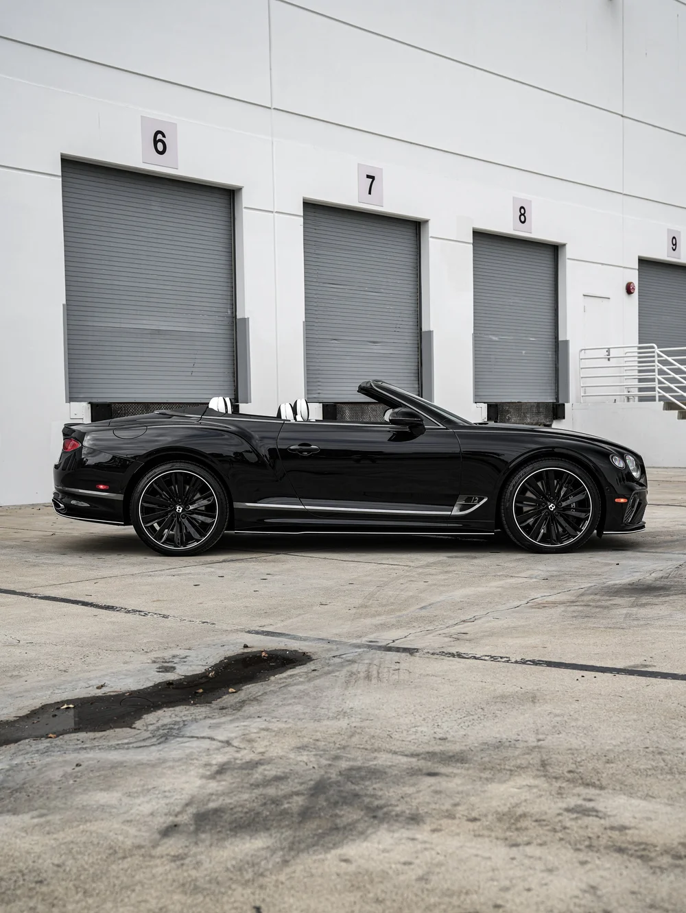 Full side profile of the Onyx Black Bentley Continental GTC with its roof down, black wheels and bright lower trim.