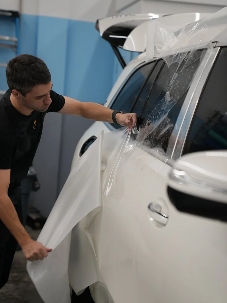 Technician positioning a broad sheet of wet clear film along the white door and upper side-body area.