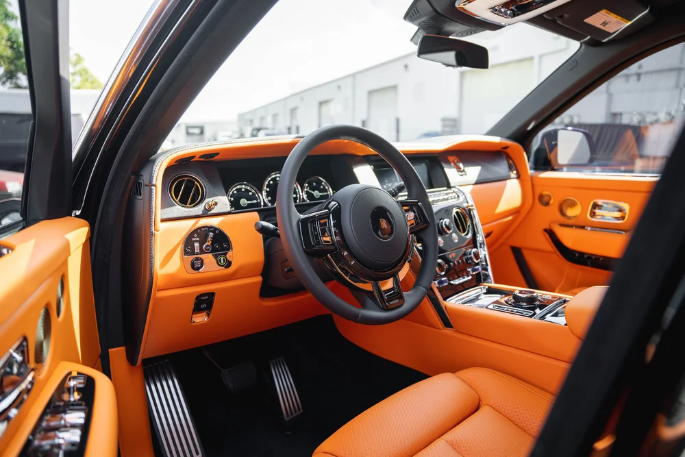 Black Rolls-Royce Cullinan with Chrome Exterior Trim — orange front-cabin upholstery, dashboard and steering wheel through the open doorway