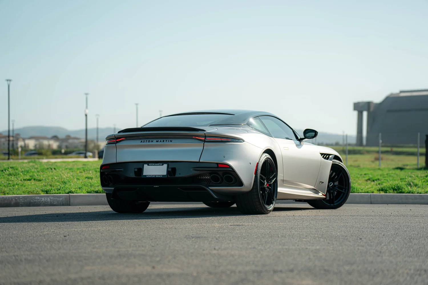 Matte-finish Aston Martin DBS in a full rear three-quarter view with black wheels, slim taillights and dark rear aero trim