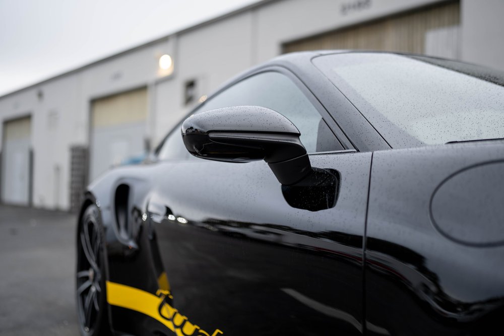 Black Porsche 911 Turbo S mirror, dark side glass and reflective door panel in low side detail