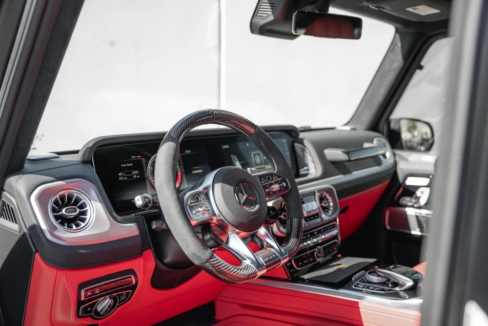 Red-and-black G 63 cabin with a patterned steering wheel, twin dashboard screens, circular vents and center-console controls