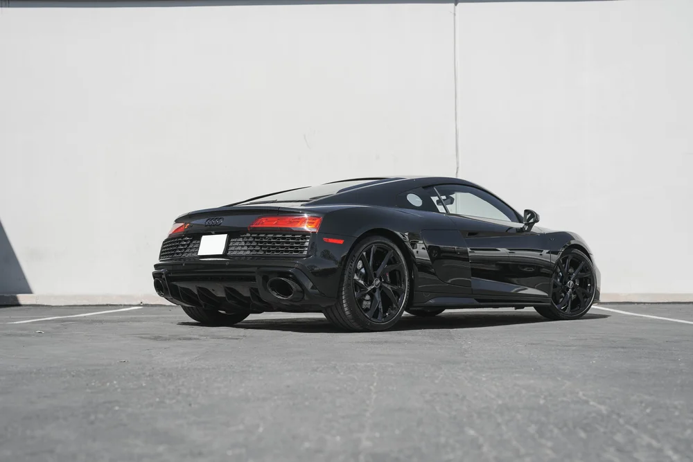 Black Audi R8 in a full rear three-quarter view with black wheels, red taillights and dark rear diffuser