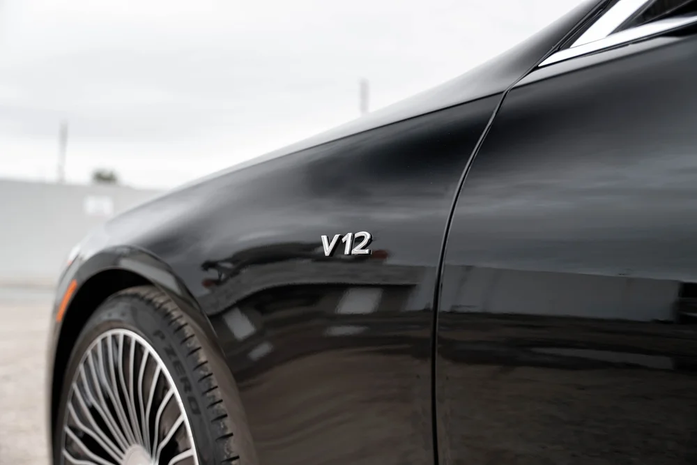 Literal V12 lettering on the reflective black front fender above part of a silver multispoke wheel