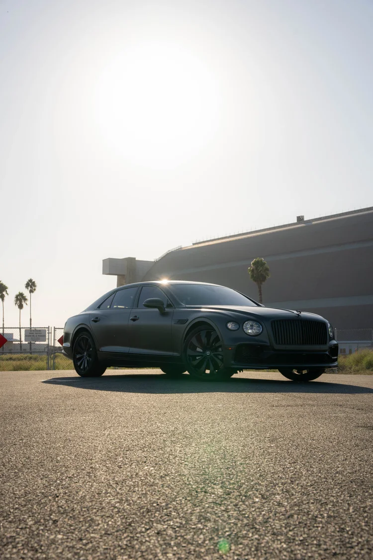 Complete front-three-quarter portrait with the matte sedan below a pale sunlit sky.