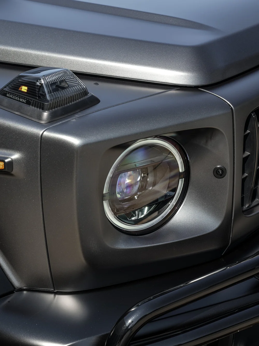 Round headlamp and fender-top indicator beside the satin grey Mercedes-AMG G 63 hood and black brush guard
