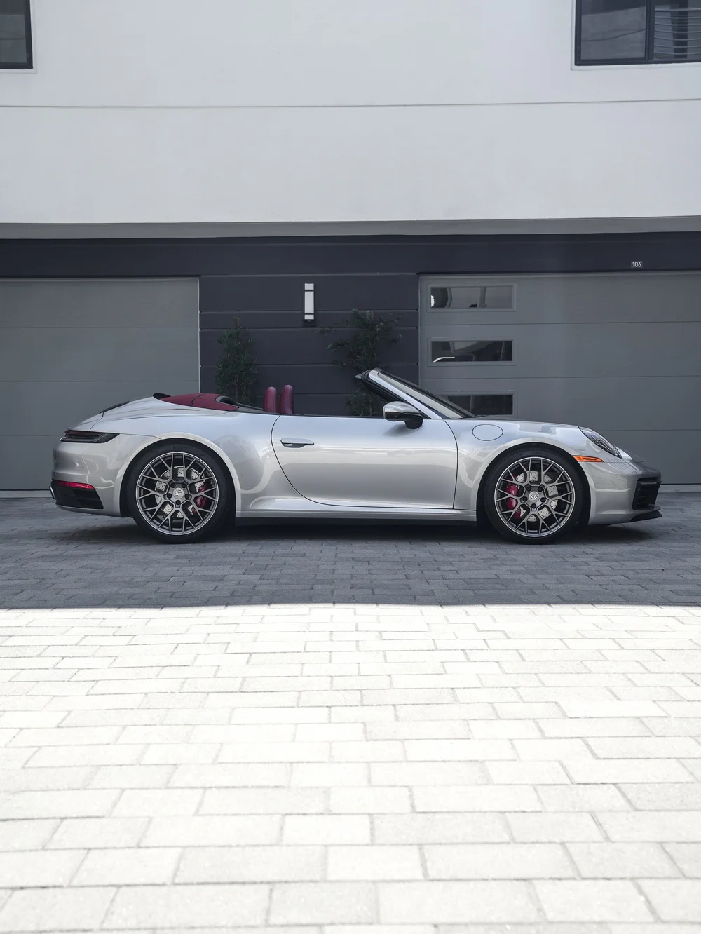 Complete side profile of the silver Porsche 911 facing right with closed doors, its roof lowered, red seat backs, multi-spoke wheels and red brake calipers.