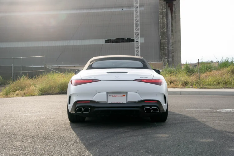 Complete straight rear view of the white SL 63 with a dark roof and four exhaust outlets centered against a sunlit industrial wall