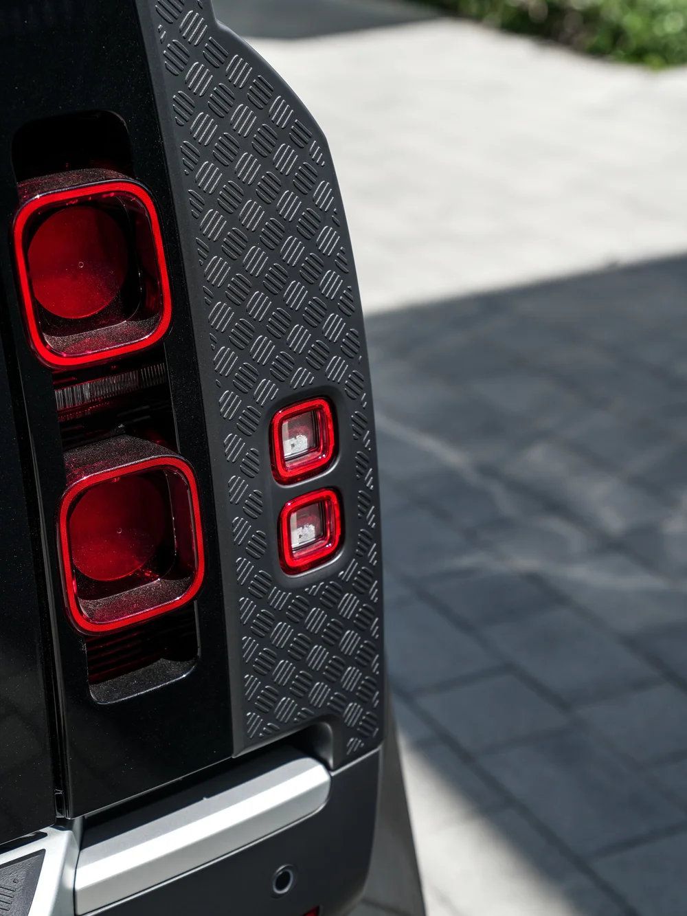 Close stacked red rear lamps beside the Defender's textured gray corner trim and dark reflective bodywork