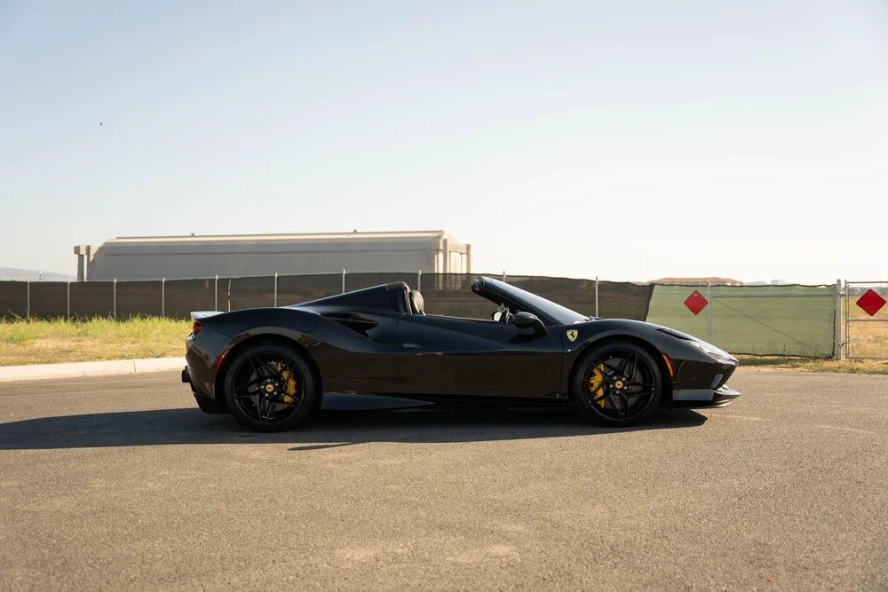 Full side profile of the black Ferrari F8 with open cockpit, sculpted side intake and black wheels