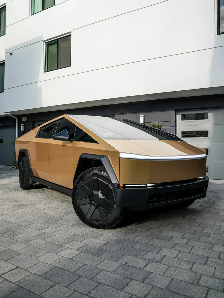 Complete gold Cybertruck in a closer front three-quarter view with wall reflections
