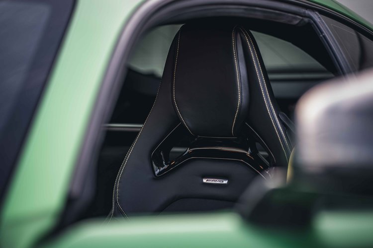 Dark sculpted seat with light stitching viewed through the open side window beside the green door frame.