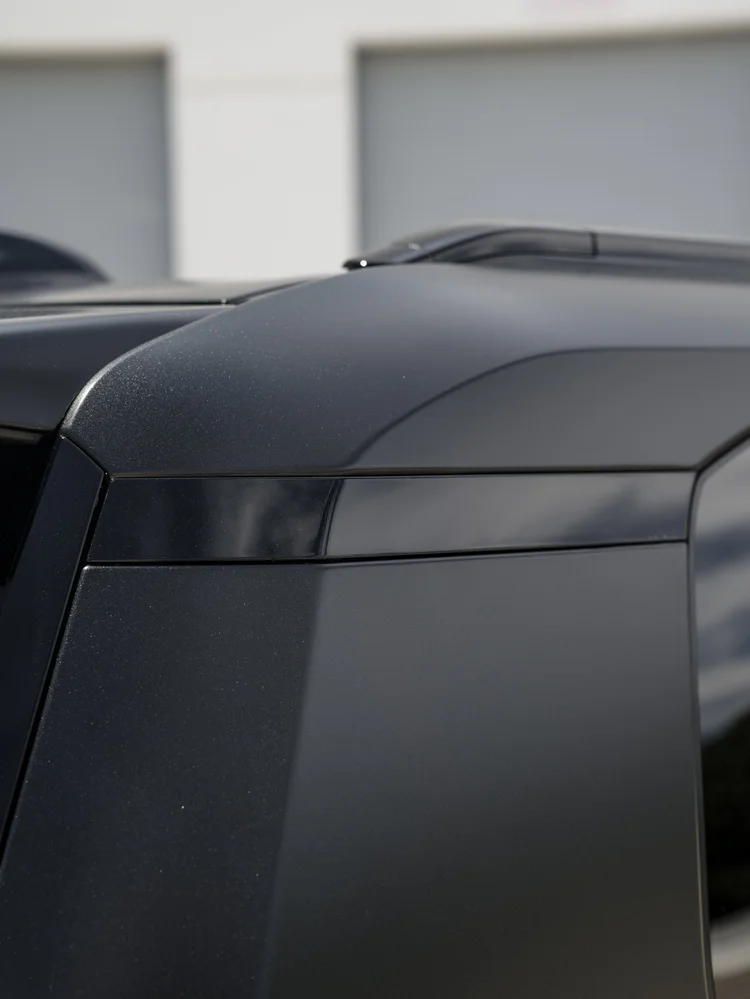 Close raised hood contour and dark front body edge with soft reflections beside a pale industrial wall