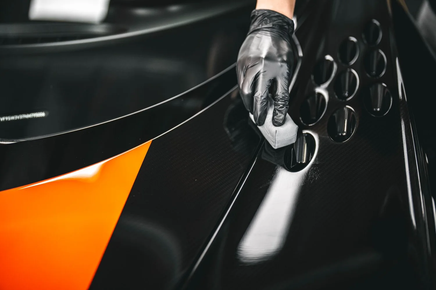 Technician preparing a black and orange vehicle surface inside Toyz Detail Studio in Irvine.