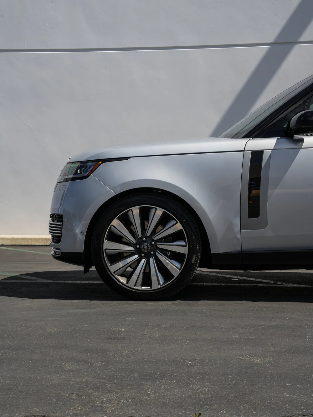 Front-wheel and fender detail of the silver Range Rover SV with part of its headlamp and side vent.