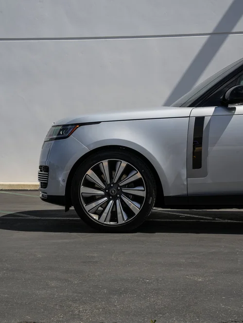 Silver Range Rover SV front-fender and wheel detail beside a grey wall, with the headlight and vertical side trim visible