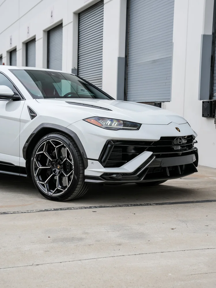 Close front-corner view of the white Urus Performante with its headlamp, front wheel, hood vent and black lower front trim.