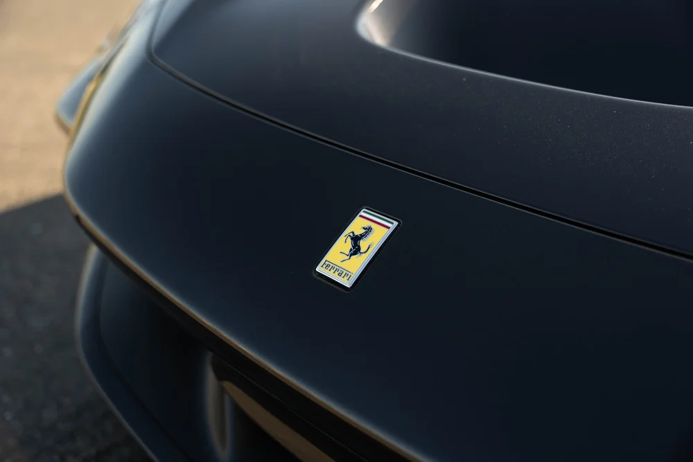 Black Ferrari F8 hood close-up with Ferrari badge, hood edge and visible paint reflections