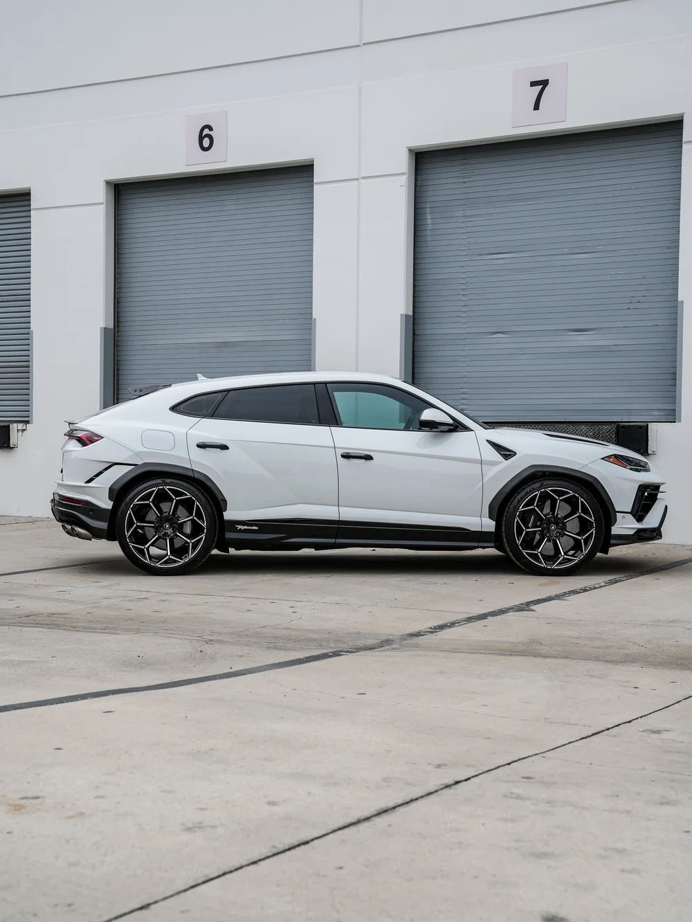 Complete side profile of the white Lamborghini Urus Performante with dark side glass, black-and-silver wheels and Performante lettering along the lower sill.