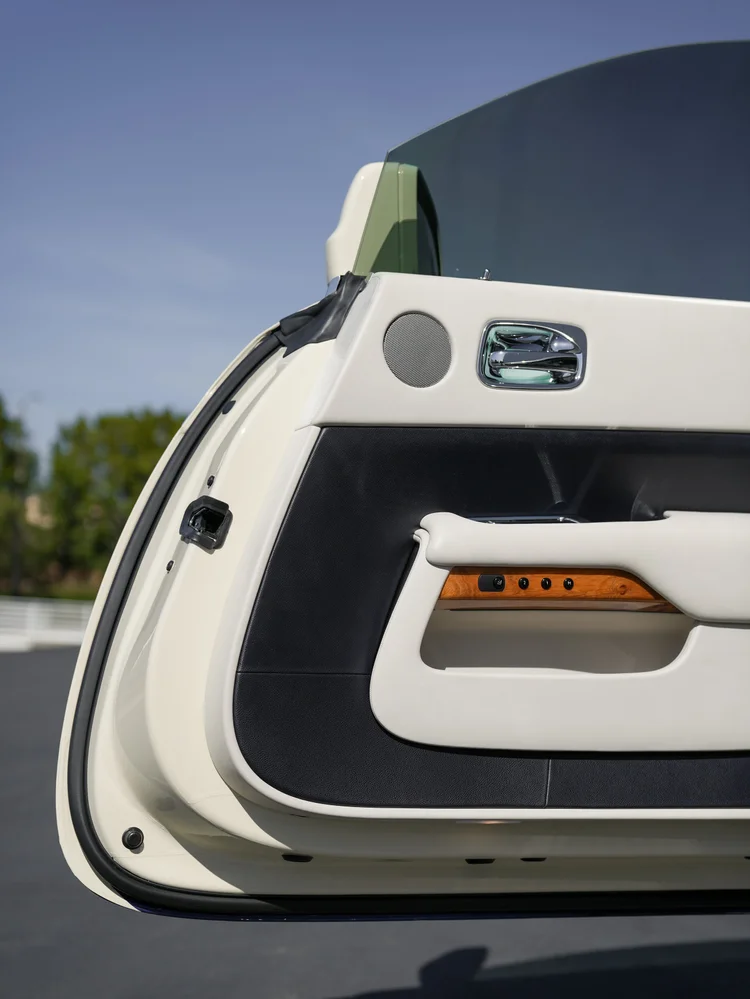 Open Rolls-Royce Wraith door panel with light and black upholstery, wood trim, speaker and chrome handle.