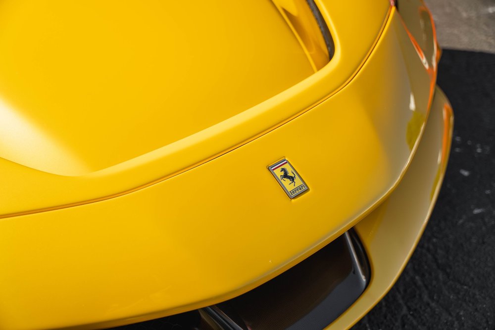 Ferrari hood badge on the yellow SF90 beside a curved panel seam and dark front air channel