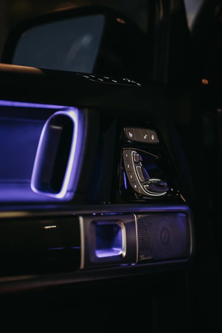 Dark door panel with purple accent lighting, silver seat-shaped controls and a round speaker grille.
