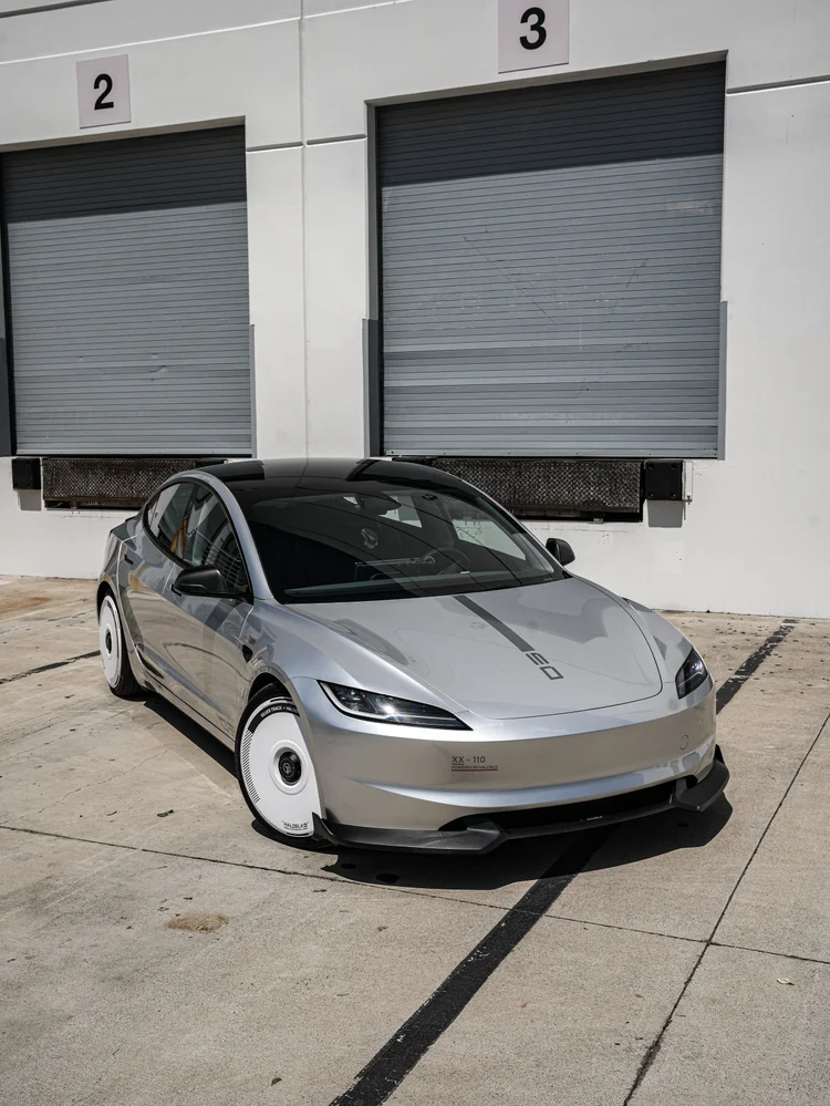 Complete silver Model 3 in a front-dominant three-quarter view, showing hood graphics, dark glass, white wheel covers and the front splitter.