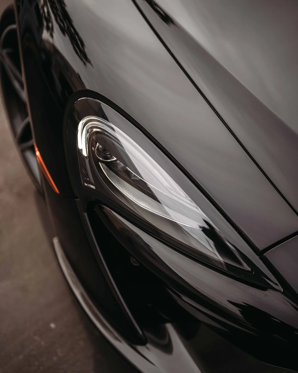 Headlamp and hood-edge close-up showing reflections across the dark front bodywork.