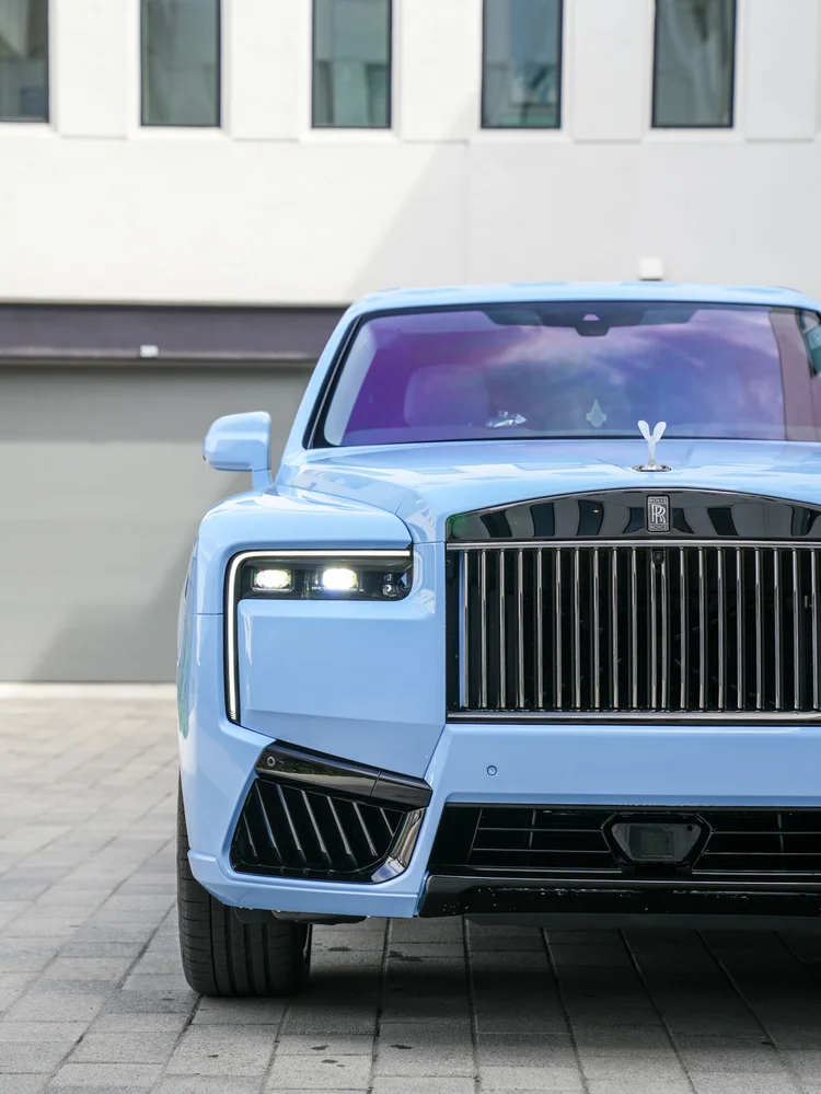 Close front view of the Powder Blue Cullinan with its dark grille, headlight, crystal hood ornament and lower intake