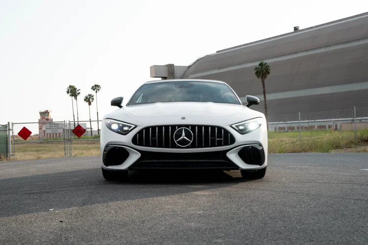 Complete low frontal view of the white SL 63 with lit headlamps, a Mercedes-star vertical-bar grille and dark lower openings