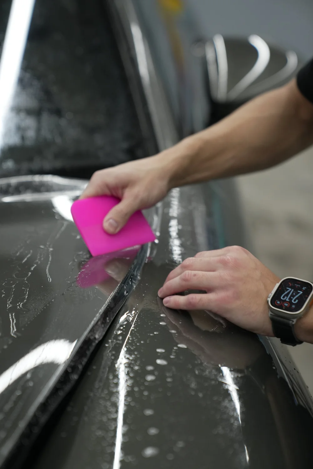 Pink squeegee working across wet clear film on a dark body panel