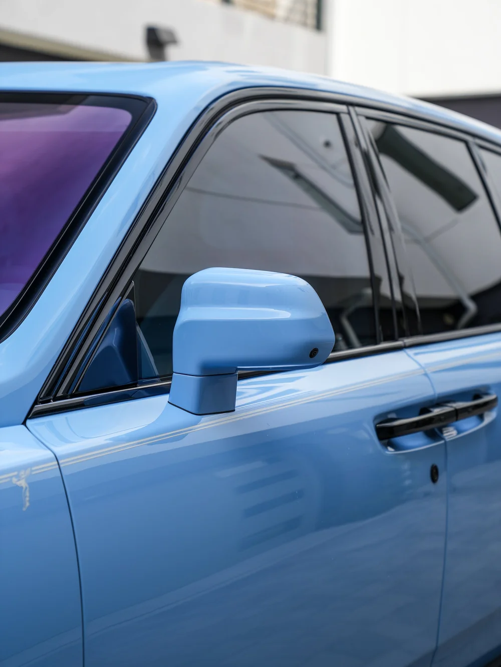 Powder Blue Cullinan side mirror and door handle below dark side windows and black window trim