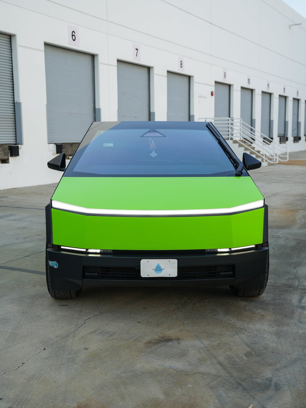Straight front view of the green Cybertruck with a white lamp strip, green hood and face, dark windshield, mirrors and black bumper.