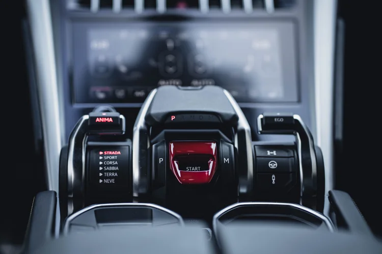 Close center-console controls with a red start-button cover, drive-mode lettering and silver-edged switches.