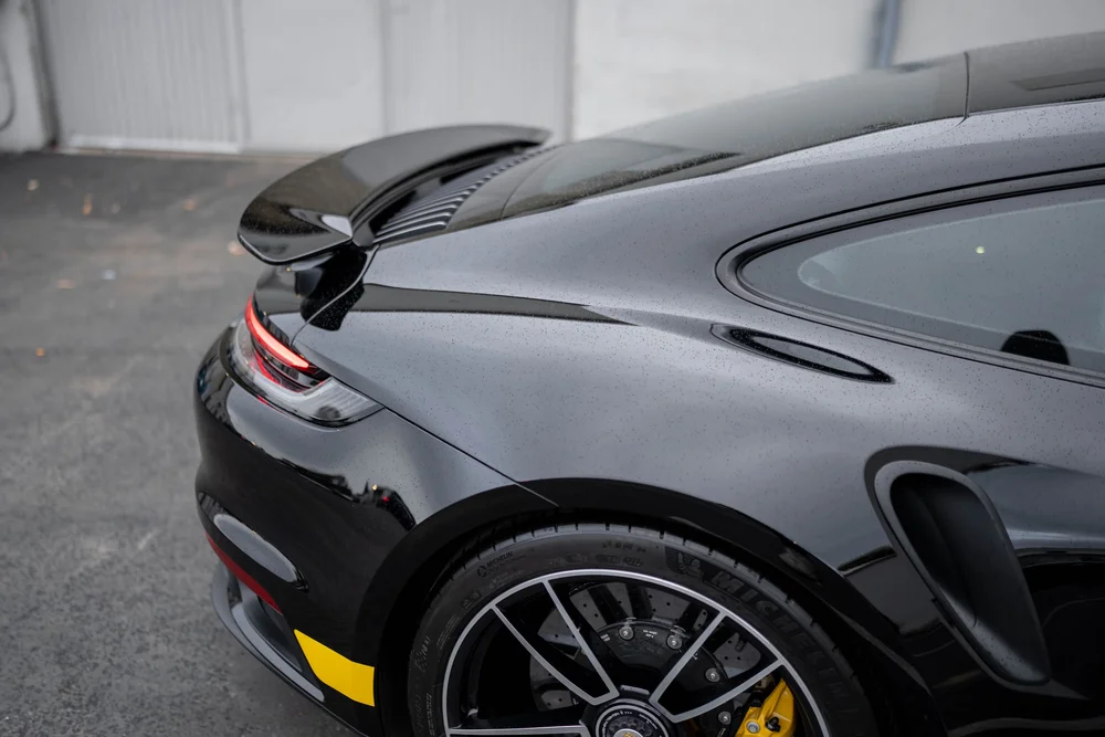 Black Porsche 911 Turbo S rear-quarter detail with raised spoiler, quarter glass, side intake and wheel