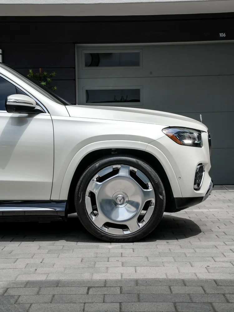 Close view of the white front quarter, mirror, front wheel, headlamp, hood ornament and chrome side step.