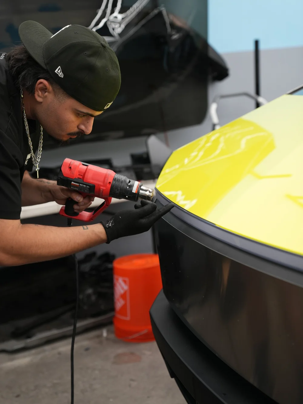 A gloved hand and red heat tool beside loose yellow vinyl at the Tesla Cybertruck front panel edge during installation.