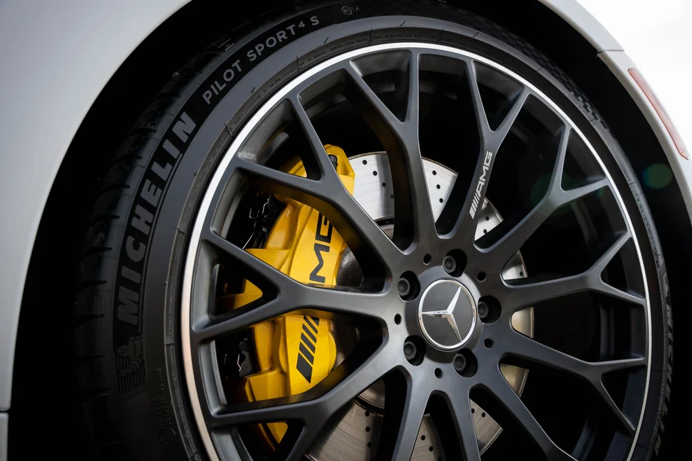 Dark multispoke wheel with a Mercedes-star center, yellow AMG-lettered caliper and a perforated brake disc