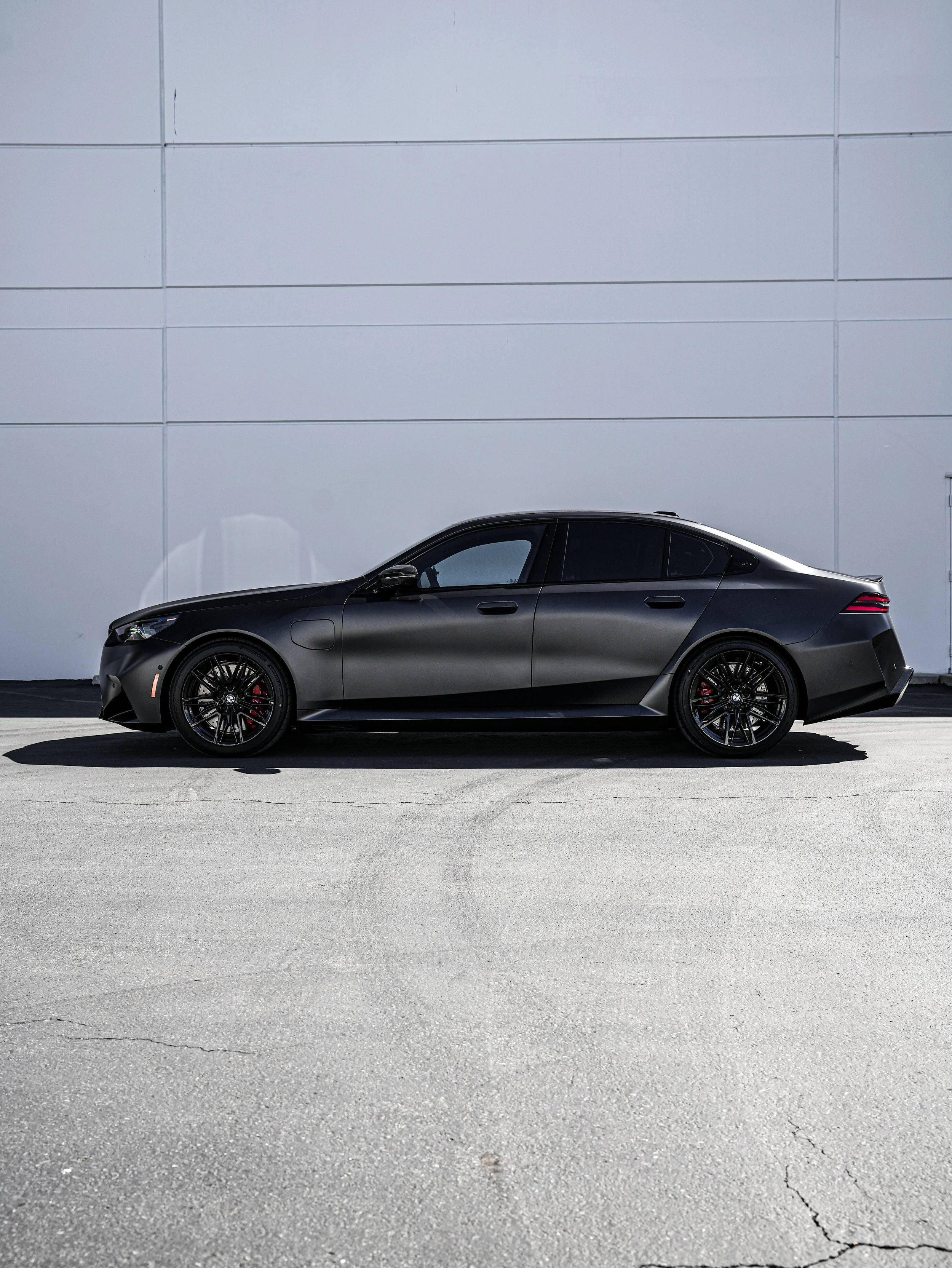 Black modern sedan parked on a concrete surface against a white wall.