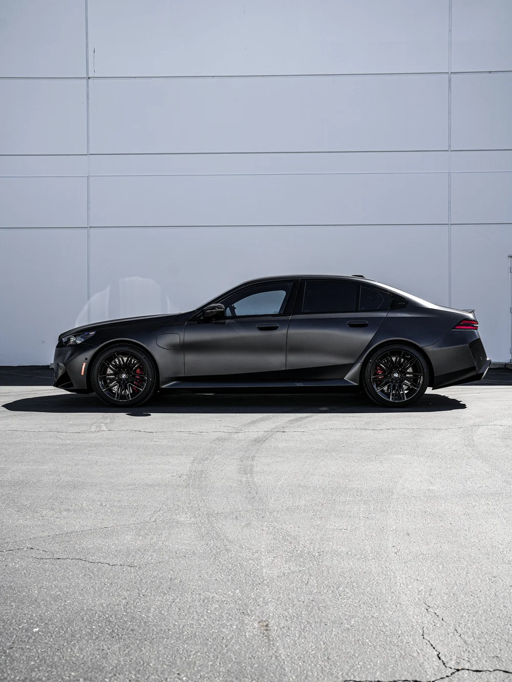BMW G90 M5 in full side profile against a gray wall, with both black wheels and dark side windows visible