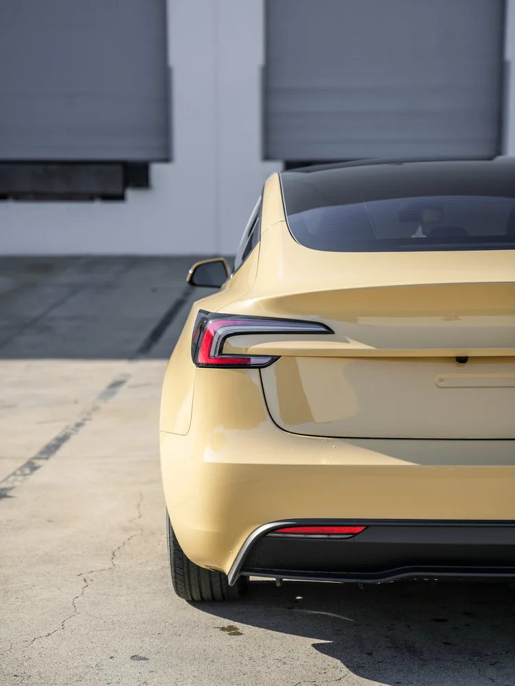 Tesla Model 3 in gloss Sunrise Yellow vinyl wrap, left rear light and bumper detail