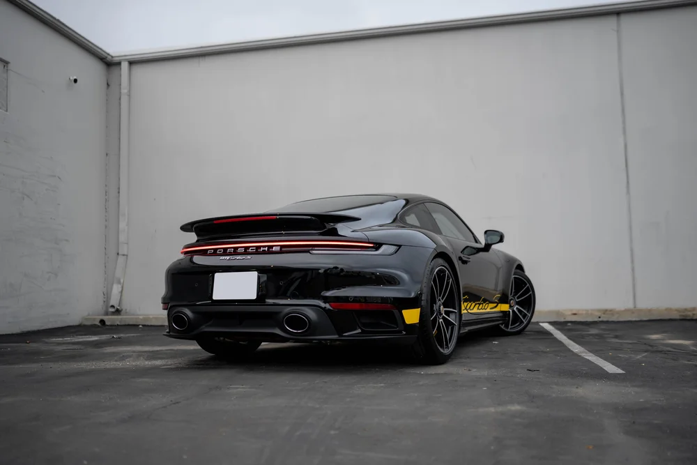 Black Porsche 911 Turbo S in rear three-quarter view with raised spoiler and yellow Turbo S side graphic