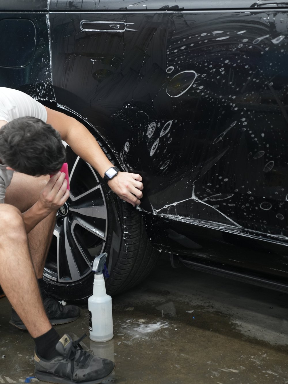 Technician positioning wet film around the rear wheel arch and lower side of the black Range Rover.