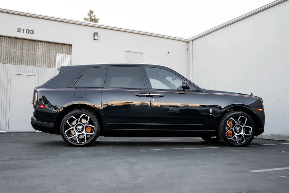 Black Rolls-Royce Cullinan Black Badge — full SUV side profile with orange coachline, bright wheel faces and orange brake calipers