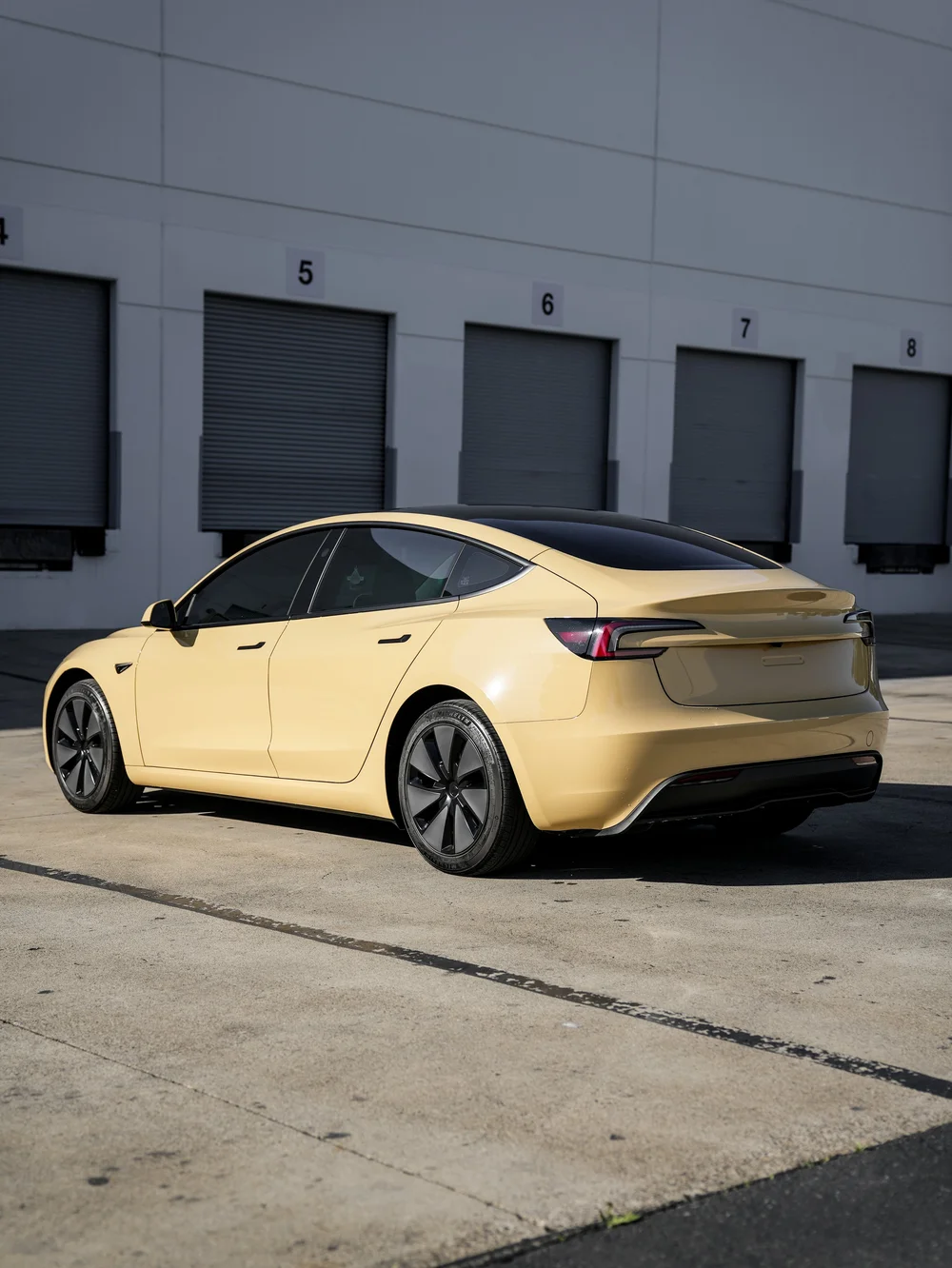 Tesla Model 3 in gloss Sunrise Yellow vinyl wrap, rear three-quarter view of the complete vehicle