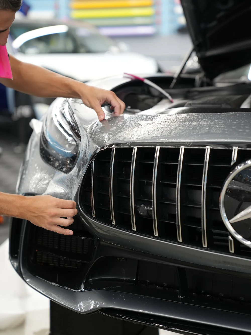 Technician installing paint protection film around a Mercedes grille and headlight